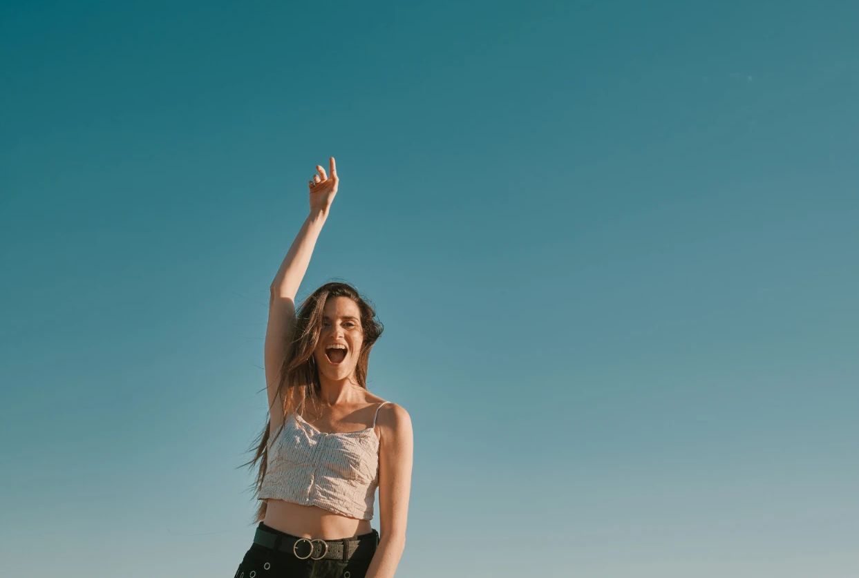 A woman smiling with one arm raised to the sky